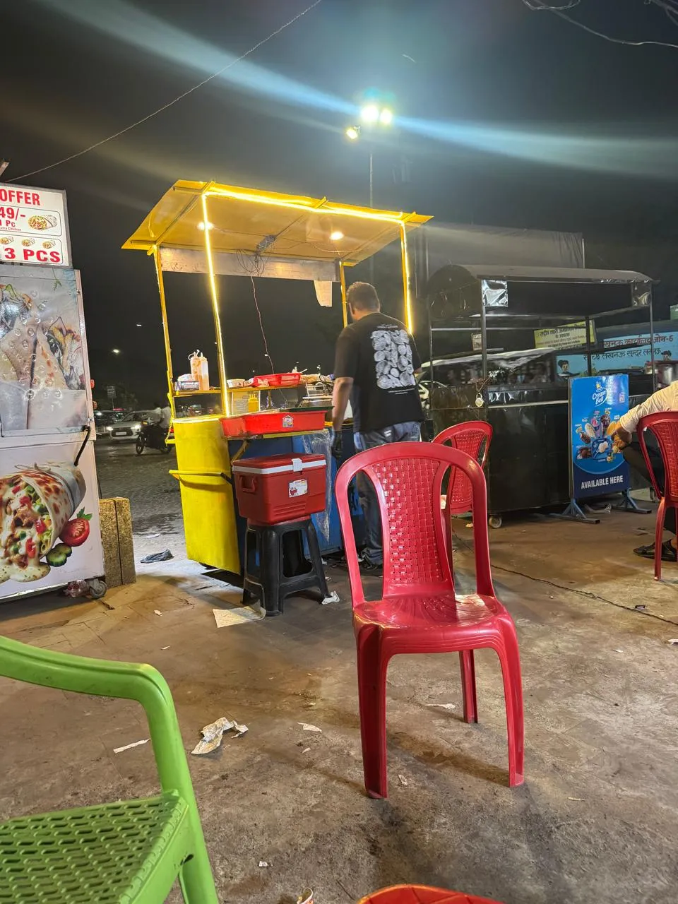 The yellow-lit Broast Nation cart at night near Ghanta Ghar, with chairs for customers